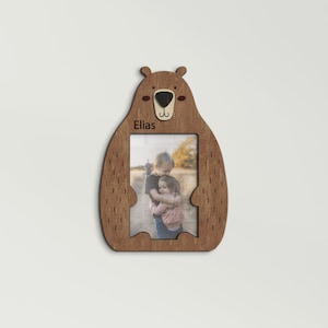 Wooden 4 by 6 inches photo frame in the shape of a cute sitting bear holding a photo. The name is engraved above the photo. This frame is 10 by 7 inches and 8 millimeters thick. The bear can be painted in different colors. The name can be changed.