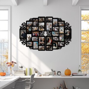 Op de afbeelding: Een zwarte, ovale fotocollage met meerdere rechthoekige frames, elk met een foto. De collage is versierd met decoratieve bladvormige uitsparingen. De setting is een licht kantoor met witte bureaus en grote ramen.