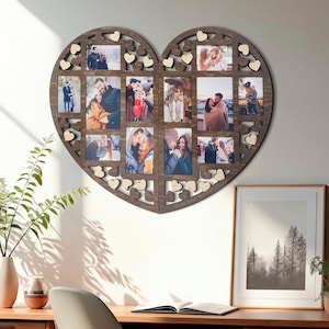 Puede incluir: Un gran marco de fotos de madera en forma de corazón con múltiples aberturas para fotos. El marco es de color marrón oscuro con pequeños detalles de corazón de madera. El marco está colgado en una pared blanca.
