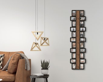 May include: A brown leather sofa with a checkered throw pillow sits in a living room with a wooden photo frame with a ruler and multiple pictures. The frame is hanging on a white wall with three wooden triangle pendant lights.