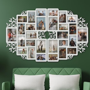Może przedstawiać: Biała ramka ścienna na wiele zdjęć z dekoracyjnym wzorem liści. Ramka mieści liczne zdjęcia o różnych rozmiarach, ułożone w owalny kształt. Ramka jest zamontowana na ciemnozielonej ścianie nad zieloną sofą.