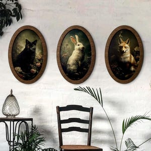 May include: Three framed oval animal portraits on a white wall. The portraits depict a black cat, a white rabbit, and a fox. The frames are wooden. The artwork is in a vintage style.