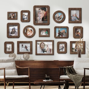 Op de afbeelding: Een verzameling bruine houten fotolijsten van verschillende formaten en vormen, gerangschikt op een witte muur. De lijsten bevatten foto's van mensen en scènes. De opstelling omvat rechthoekige, vierkante en ronde lijsten, wat een galerijmuureffect creëert.