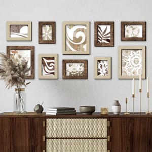 Könnte beinhalten: Eine Wandgalerie mit neun gerahmten Drucken mit abstrakten Mustern in Braun-, Beige- und Weißtönen. Die Rahmen sind aus Holz mit einer hellbraunen Oberfläche. Die Galerie wird über einem Holz-Konsolentisch mit einer geflochtenen Rattanfront präsentiert.