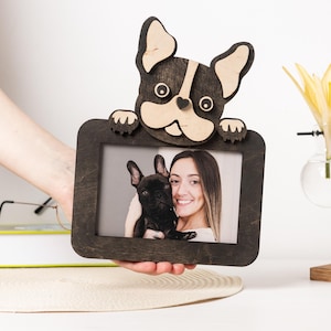 Könnte beinhalten: Ein Holz-Bilderrahmen mit einem 3D-geschnitzten Französischen Bulldoggen-Design. Der Rahmen hat eine dunkelbraune Oberfläche und ein hellbraunes Interieur. Ein Foto einer Frau und eines Hundes befindet sich im Rahmen.