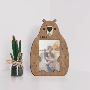Wooden 4 by 6 inches photo frame in the shape of a cute sitting bear holding a photo. The name is engraved above the photo. This frame is 10 by 7 inches and 8 millimeters thick. The bear can be painted in different colors. The name can be changed.