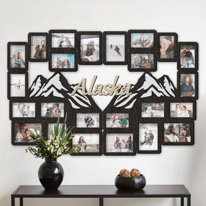 Könnte beinhalten: Eine schwarze Holz-Fotocollage mit mehreren Bilderrahmen in ovaler Form. Das Wort "Alaska" ist aus hellem Holz ausgeschnitten. Die Collage ist mit Berg-Ausschnitten und einer schwarzen Vase mit Blumen dekoriert.