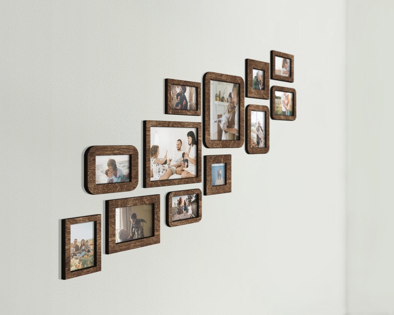 K&ouml;nnte beinhalten: Eine Anordnung von zehn Holzbilderrahmen unterschiedlicher Gr&ouml;&szlig;e an einer wei&szlig;en Wand. Die dunkelbraunen Rahmen enthalten Fotos von Menschen. Die Rahmen sind in einem diagonalen Muster angeordnet.
