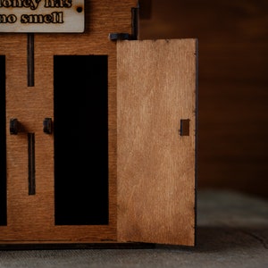 Puede incluir: Una caja de madera con dos compartimentos abiertos y una puerta que dice "El dinero no huele".