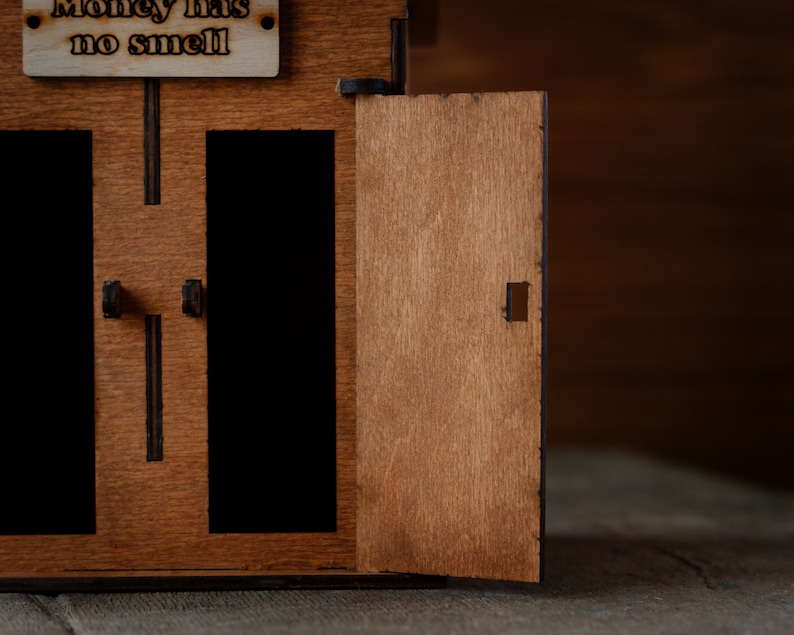 Puede incluir: Una caja de madera con dos compartimentos abiertos y una puerta que dice "El dinero no huele".