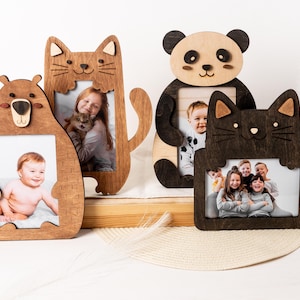Puede incluir: Tres marcos de fotos de madera con forma de oso, gato y panda. Cada marco tiene un recorte de la cara del animal y un espacio para una foto. Los marcos son de diferentes colores y tienen un aspecto rústico.