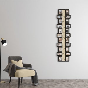 May include: A black wooden photo frame with a built-in ruler, designed to hold 16 photos. The frame is hanging on a white wall, with a gray armchair and a black floor lamp in the foreground.