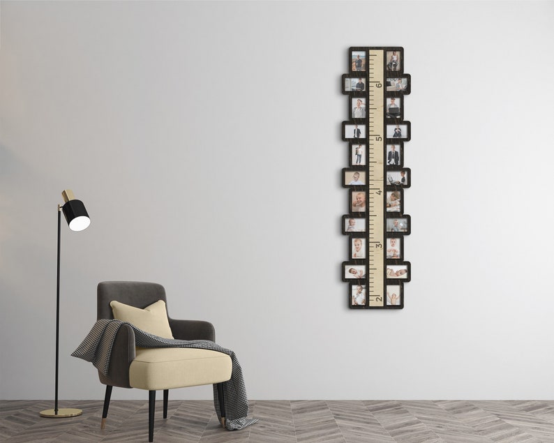 May include: A black wooden photo frame with a built-in ruler, designed to hold 16 photos. The frame is hanging on a white wall, with a gray armchair and a black floor lamp in the foreground.