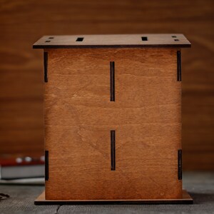 Puede incluir: Una caja de madera con un tinte marr&oacute;n y una ranura en la parte superior. La caja tiene un dise&ntilde;o simple con l&iacute;neas negras en la parte delantera.