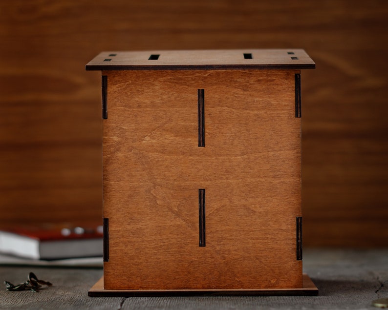 Puede incluir: Una caja de madera con un tinte marr&oacute;n y una ranura en la parte superior. La caja tiene un dise&ntilde;o simple con l&iacute;neas negras en la parte delantera.