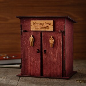 May include: A wooden piggy bank shaped like a outhouse with a sign that reads "Money has no smell".