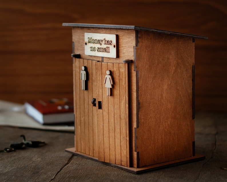 Puede incluir: Caja de madera para guardar dinero con forma de letrina con un letrero que dice "El dinero no huele".