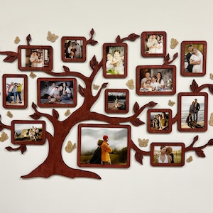Op de afbeelding: Een bruine houten fotolijst in de vorm van een stamboom met meerdere openingen voor foto's. De lijst is versierd met gouden vlinders en bevat foto's van families en individuen.