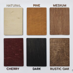 May include: A display of six rectangular wooden samples in various finishes: Natural, Pine, Medium, Cherry, Dark, and Rustic Oak. Each sample is labeled with its respective finish name in capital letters. The samples are arranged in two rows of three.