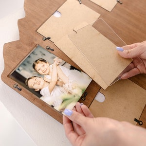 May include: A wooden photo frame with multiple openings for pictures. A person is placing a clear acrylic sheet over a photo of two children.