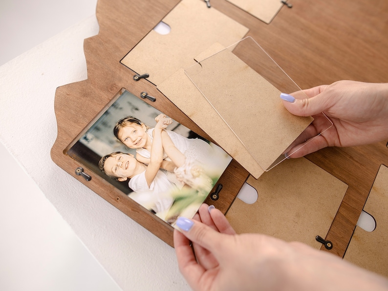 May include: A wooden photo frame with multiple openings for pictures. A person is placing a clear acrylic sheet over a photo of two children.