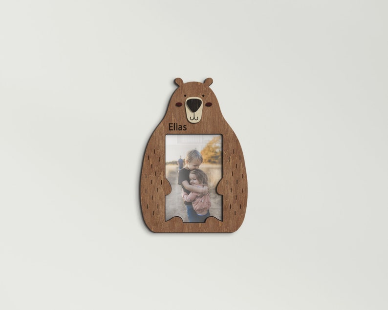 Wooden 4 by 6 inches photo frame in the shape of a cute sitting bear holding a photo. The name is engraved above the photo. This frame is 10 by 7 inches and 8 millimeters thick. The bear can be painted in different colors. The name can be changed.