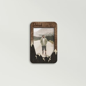 Peut inclure: Un cadre photo en bois avec un motif de silhouette de montagne. Le cadre a une découpe pour une photo et une inscription personnalisée qui dit "Daniel".