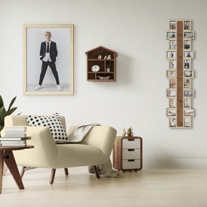 May include: A wooden photo frame with a ruler on the side and multiple slots for pictures. The frame is hanging on a white wall above a beige armchair with a black and white checkered pillow. There is a small wooden shelf with a birdhouse design on the wall above the armchair.