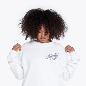 May include: White long-sleeve sweatshirt with a purple embroidered design that says "Loyalty" on the front.