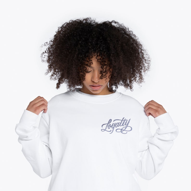 May include: White long-sleeve sweatshirt with a purple embroidered design that says "Loyalty" on the front.