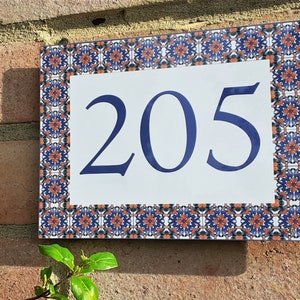 May include: A white ceramic house number sign with a blue border and a blue number "205" on a white background. The border is decorated with a repeating pattern of orange, blue, and green.