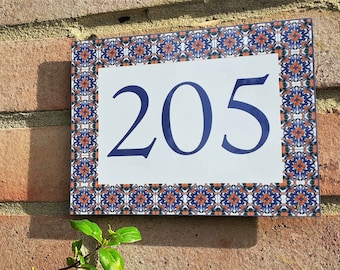May include: A white ceramic house number sign with a blue border and a blue number "205" on a white background. The border is decorated with a repeating pattern of orange, blue, and green.