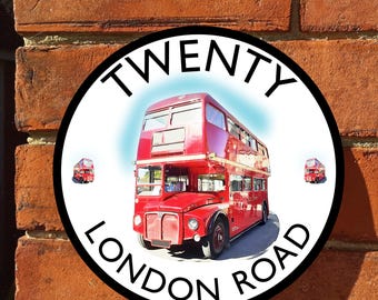 Op de afbeelding: Een rond bord met de tekst "TWENTY LONDON ROAD" rond een illustratie van een rode dubbeldekkerbus. Het bord is bevestigd aan een rode bakstenen muur. Twee kleinere busafbeeldingen zijn ook aanwezig.