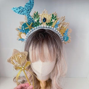 May include: A gold and blue mermaid crown headband with a blue glitter tail, white pearls, and seashells. A matching gold glitter wand with a seashell and a white pearl.