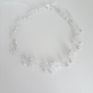 May include: A delicate white floral headband with faux pearls and a ribbon tie. The headpiece features small, translucent flowers and clusters of pearl beads, perfect for weddings or special occasions.