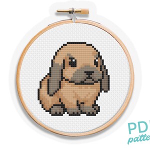 May include: A cross-stitch pattern of a brown and gray bunny rabbit in a wooden embroidery hoop. The bunny has floppy ears and is in a sitting position. The text "PDF pattern" is in the lower right corner.