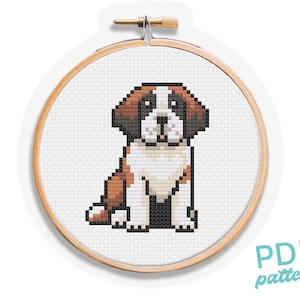 May include: A cross-stitch pattern of a Saint Bernard puppy in a wooden embroidery hoop. The puppy is depicted in brown, white, and black pixels, sitting upright. The text "PDF pattern" is in the lower right corner.