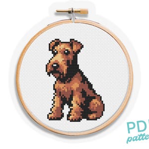 Könnte beinhalten: Ein Kreuzstichmuster eines braunen und schwarzen Airedale Terriers, der mit hochgestellten Ohren sitzt. Das Muster ist in einem hölzernen Stickrahmen dargestellt.