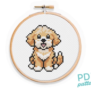 May include: Cross stitch pattern of a cute, brown and white dog with a pink tongue. The pattern is in a wooden embroidery hoop.