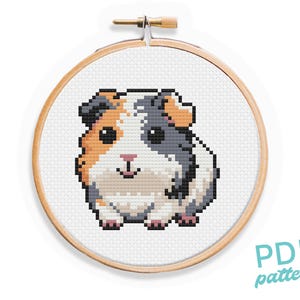 May include: Cross stitch pattern of a cute guinea pig with brown, white, and gray fur. The guinea pig is looking at the viewer with a friendly expression. The pattern is in a round wooden embroidery hoop.
