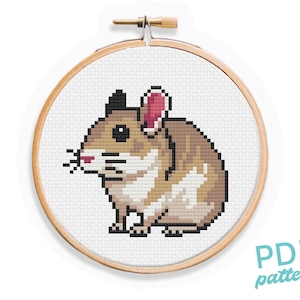 May include: Cross stitch pattern of a brown and white hamster with pink ears, in a wooden embroidery hoop. The pattern is available as a PDF download.