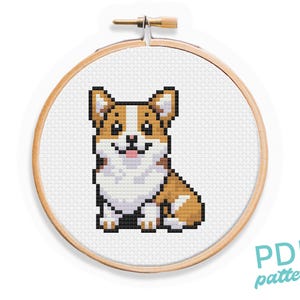 May include: A cross-stitch pattern of a brown and white corgi dog sitting with its tongue sticking out. The pattern is in a wooden embroidery hoop.