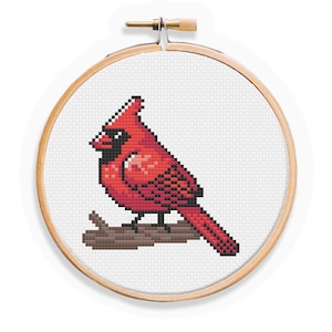 May include: A red cardinal bird cross-stitch pattern in a wooden embroidery hoop. The bird is perched on a branch with its wings folded.
