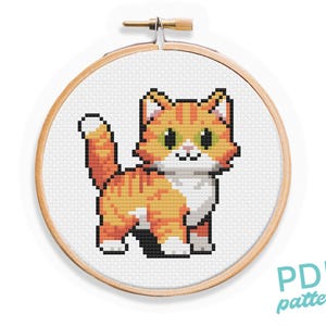 Op de afbeelding: Kruissteekpatroon van een oranje-witte kat met groene ogen. De kat zit op een witte achtergrond en is omringd door een houten borduurring.