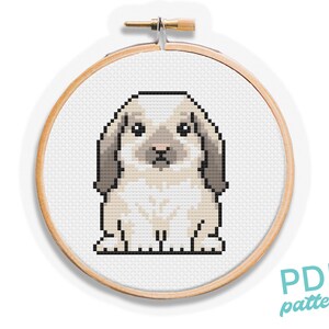 May include: Cross-stitch pattern of a light beige bunny with floppy ears, in a wooden embroidery hoop. The bunny is made of pixelated stitches. The text "PDF pattern" is in the lower right corner.