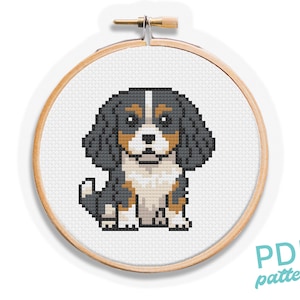 Puede incluir: Un patrón de punto de cruz de un perro Cavalier King Charles Spaniel en un bastidor de bordado de madera. El perro está representado en un estilo pixelado con colores negro, marrón y blanco. El texto "PDF pattern" es visible.