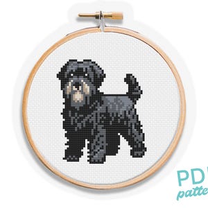 Op de afbeelding: Een kruissteekpatroon van een zwarte hond met een bruine snuit, weergegeven in een houten borduurring. De hond is weergegeven in een pixelachtige stijl. De woorden "PDF pattern" zijn gedrukt in turquoise.