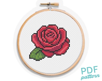 May include: A cross-stitch pattern of a red rose with green leaves, displayed in a wooden embroidery hoop. The design is pixelated, with the text "PDF pattern" in the lower right corner.