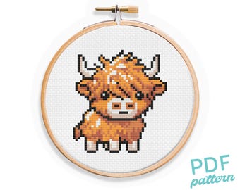 May include: A cross-stitch pattern of a Highland cow in an embroidery hoop. The cow is orange and white with black accents. The text "PDF pattern" is in the lower right corner.