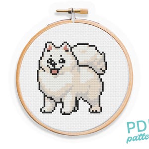 May include: A cross-stitch pattern of a white fluffy dog with a pink nose and tongue, in a wooden embroidery hoop. The pattern is labeled "PDF pattern".